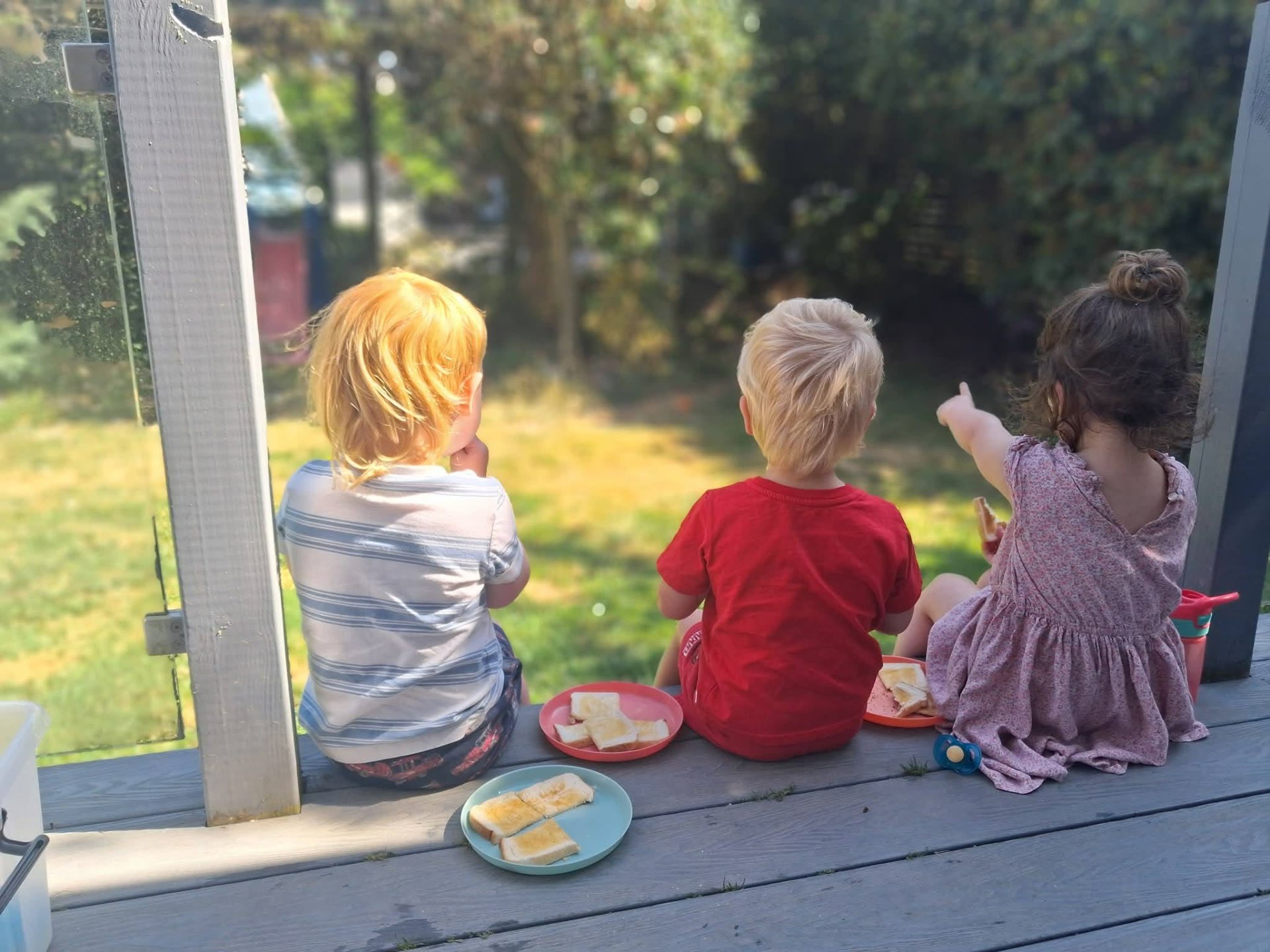 Children sitting on a sunny garden deck enjoying a snack together